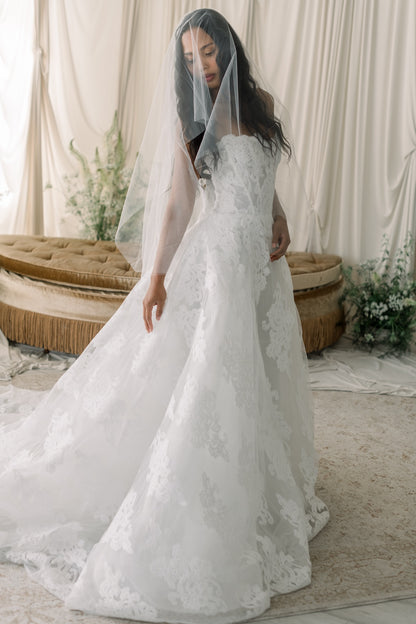 Woman in a white lace wedding dress with a veil in a softly lit room.