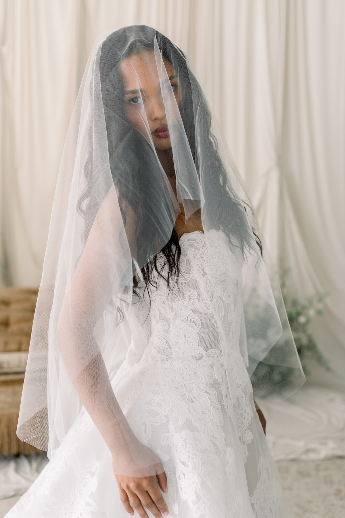 Woman wearing a white wedding dress with a sheer veil in a softly lit room.