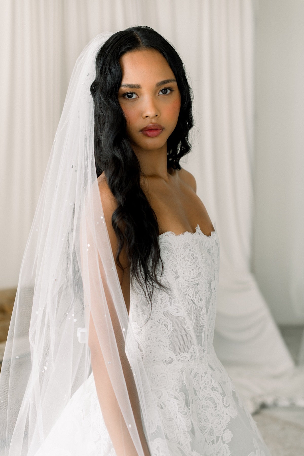 Woman wearing a white wedding dress with a long veil against a neutral background