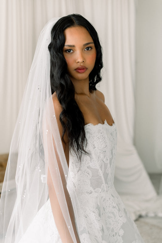 Woman wearing a white wedding dress with a long veil against a neutral background