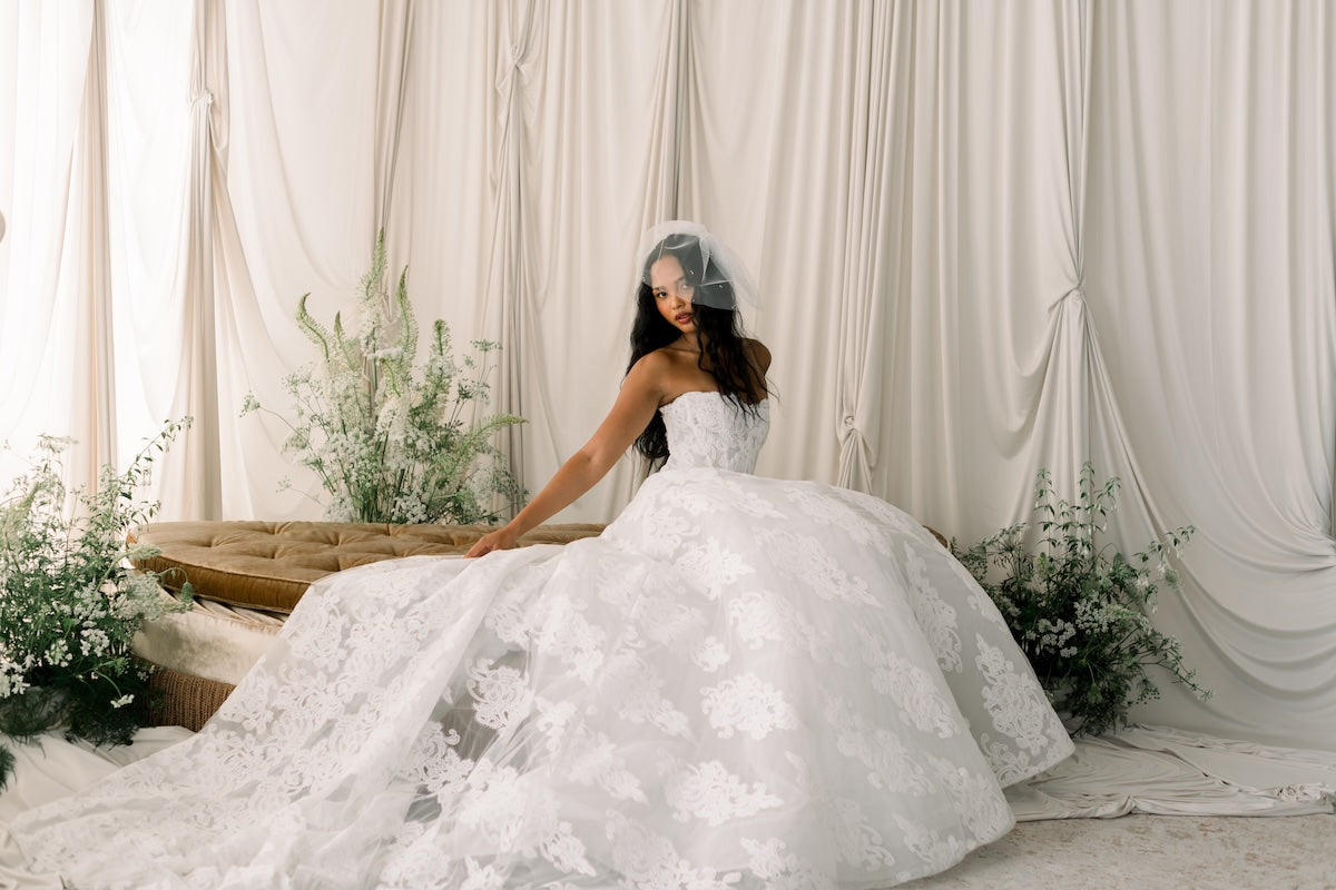 Bride in a white wedding dress sitting in a decorated room with flowers and curtains.