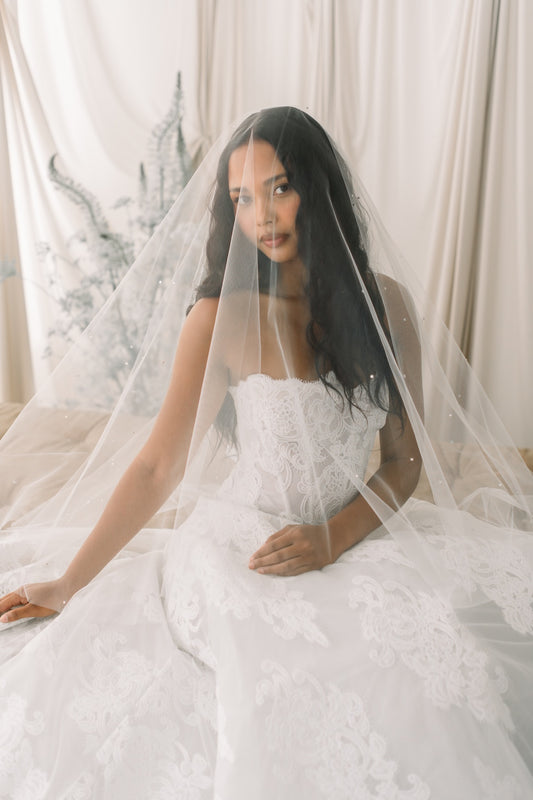 Woman in a white wedding dress with a veil sitting on a bed.