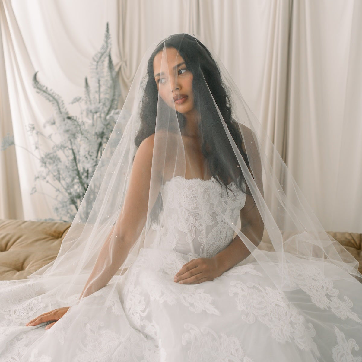 Woman in a white wedding dress with a veil sitting in a softly lit room.