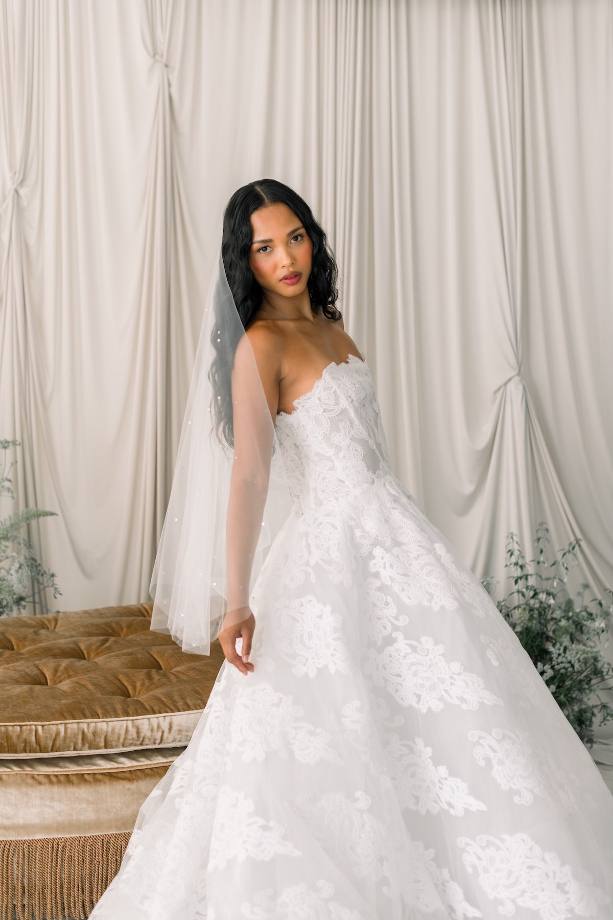 Woman in a white wedding dress standing against a white curtain backdrop