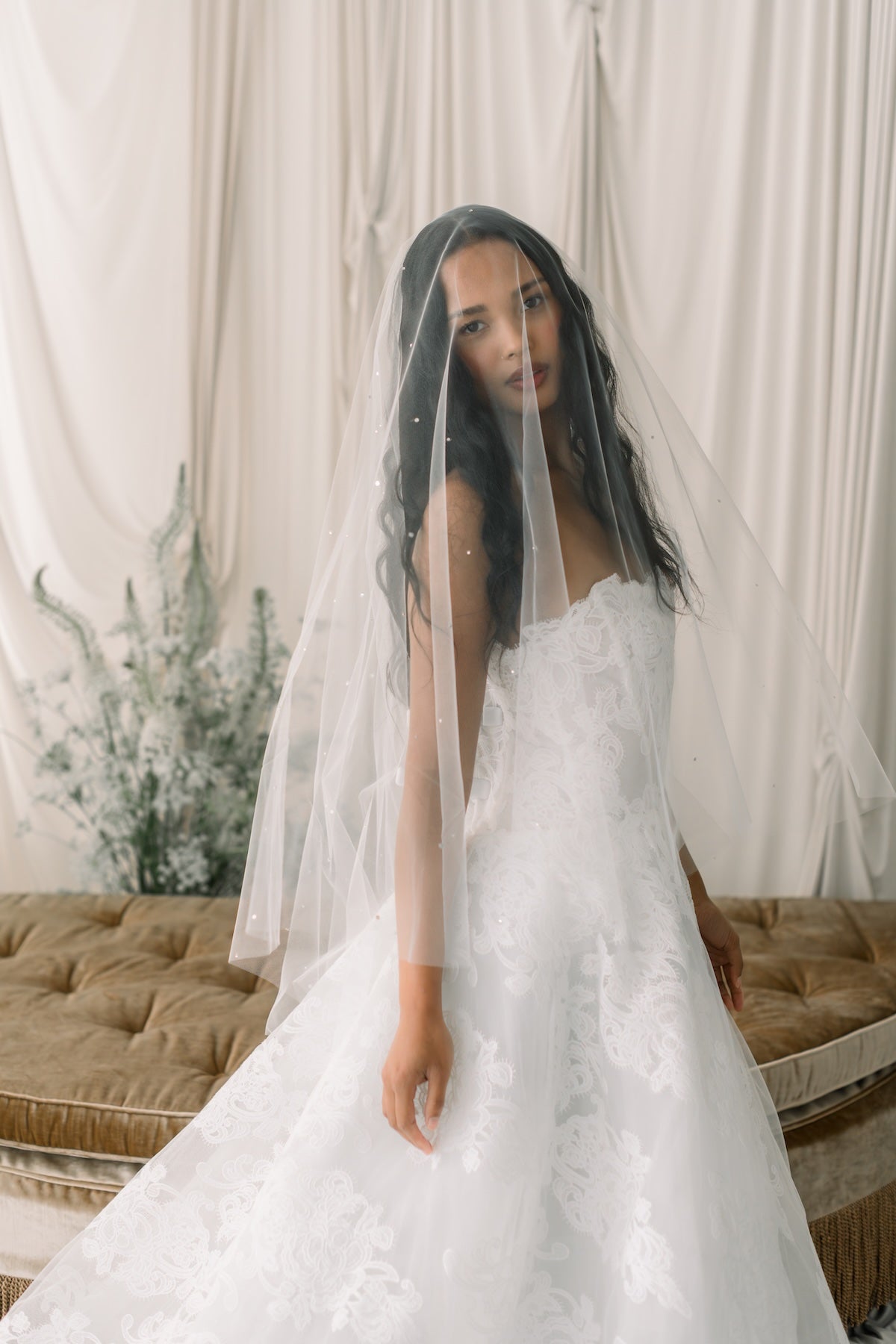 Woman in a white wedding dress with a veil standing in front of a neutral background