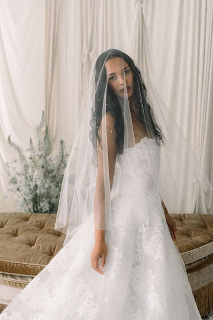Woman in a white wedding dress with a veil standing in front of a neutral background