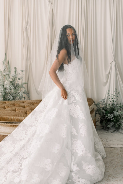 Woman in a white wedding dress standing in a decorated room with curtains and plants.