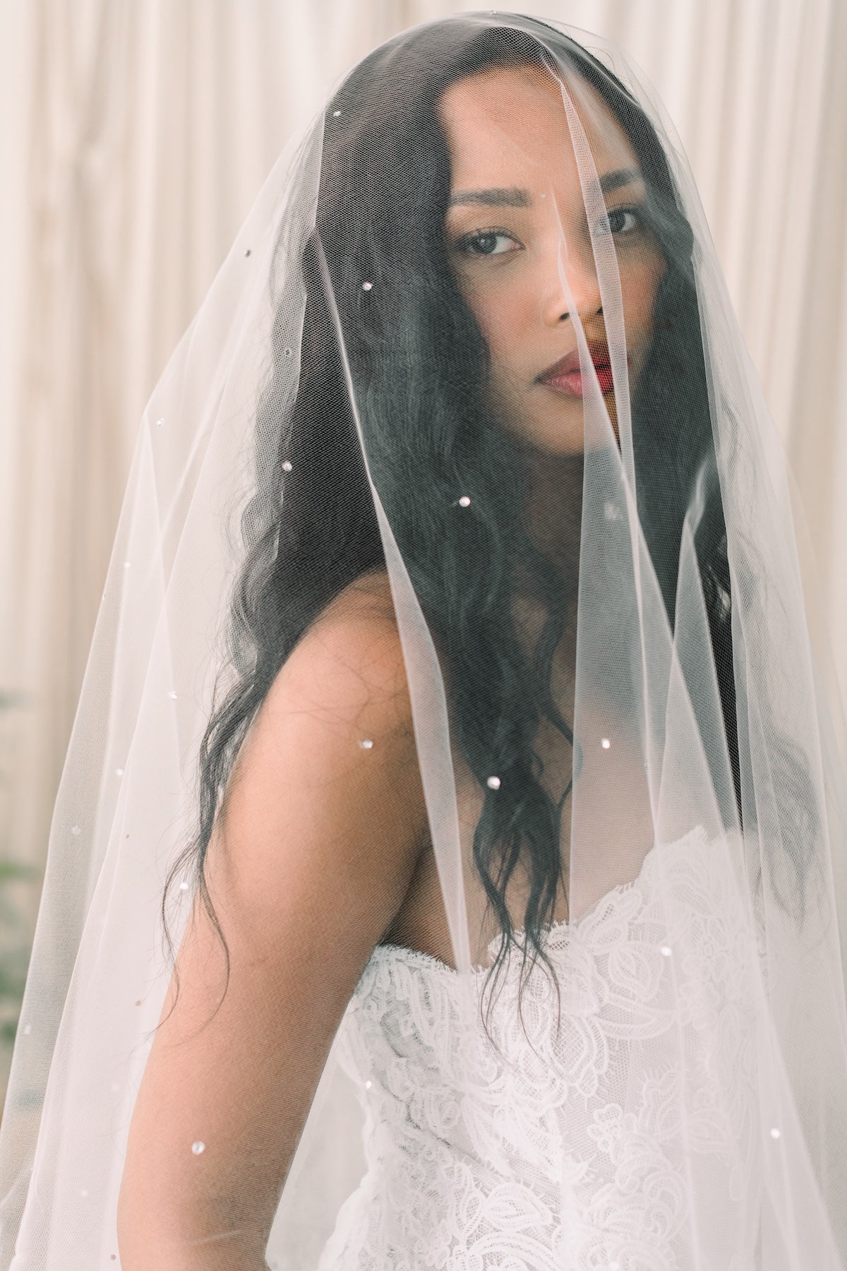 Woman wearing a white wedding dress with a veil against a neutral background