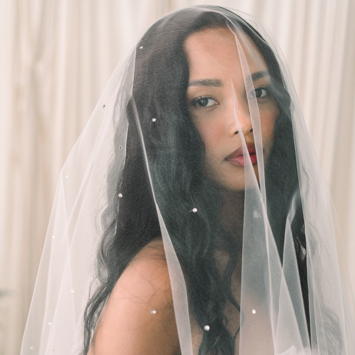 Woman wearing a white wedding dress with a veil against a neutral background
