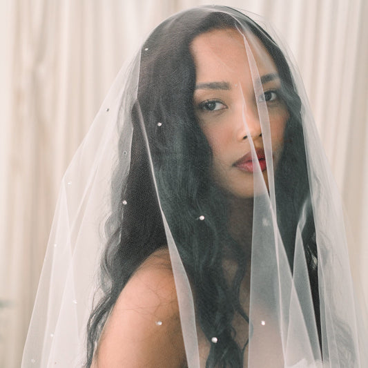 Woman wearing a white wedding dress with a veil against a neutral background