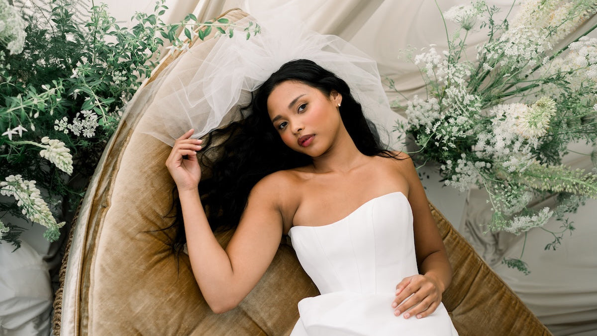 Woman in a white wedding dress sitting on a decorative chair with flowers around her.