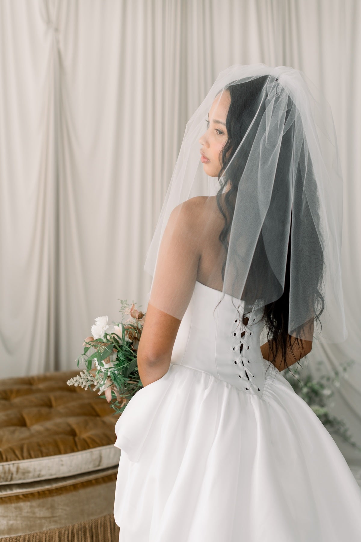 Woman in a white wedding dress with a veil standing against a neutral background