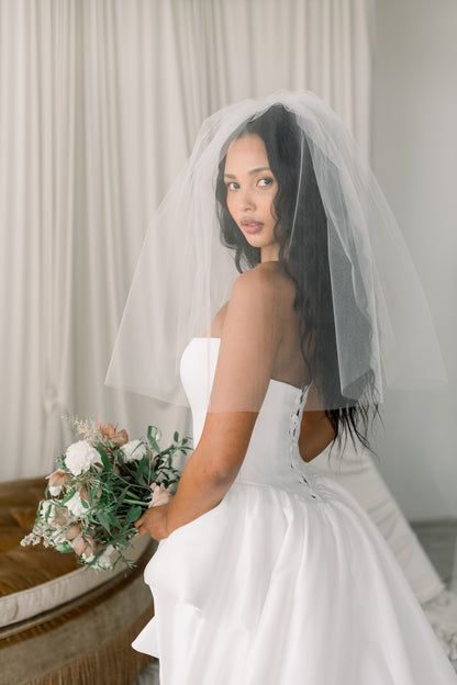 Bride in a white dress with a veil holding a bouquet indoors.