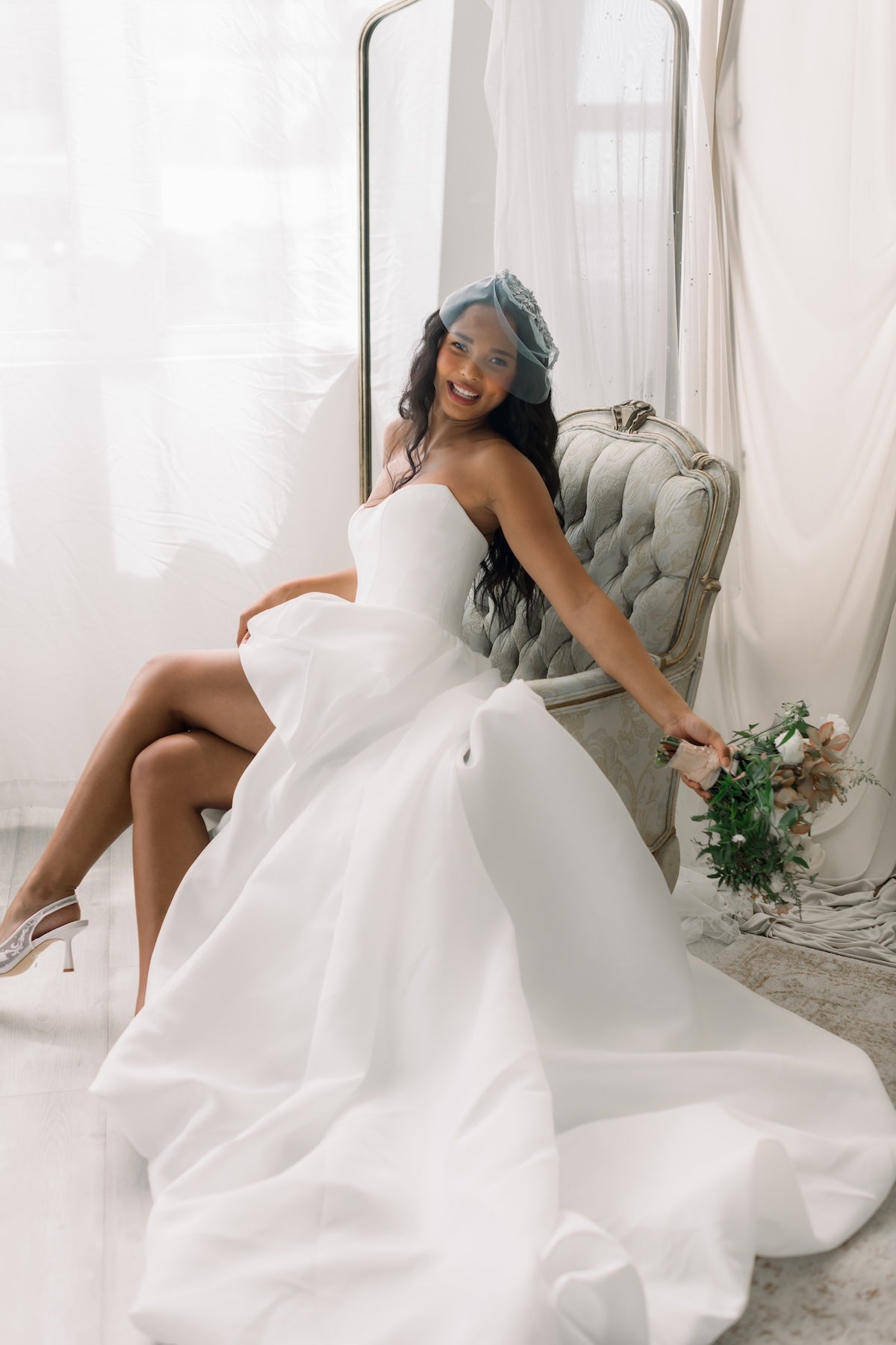 Woman in a white wedding dress sitting on a chair holding a bouquet.