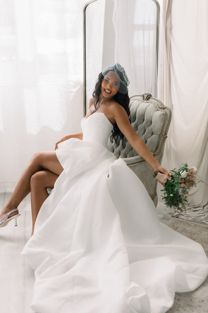 Woman in a white wedding dress sitting on a chair holding a bouquet.