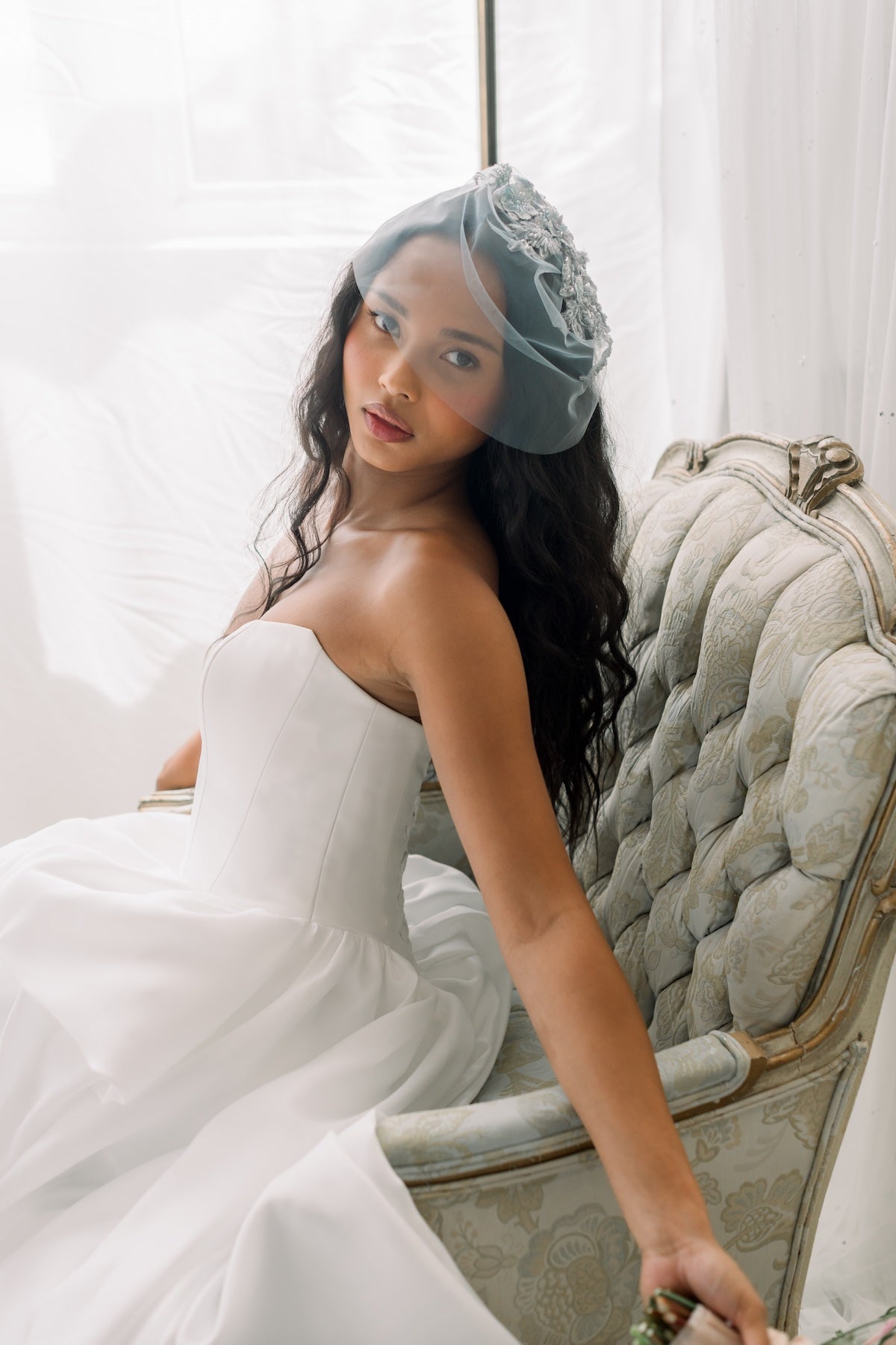 Woman in a white dress with a blue veil sitting on an ornate chair.