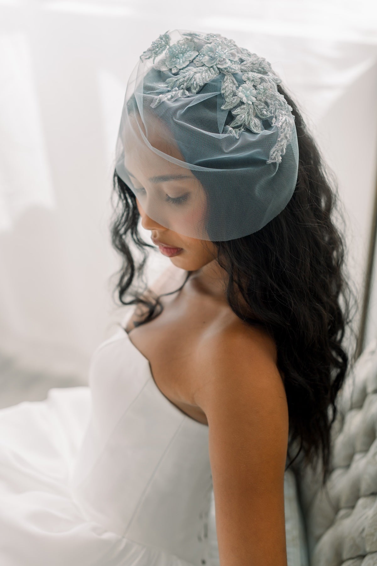 Woman wearing a light blue veil with floral lace details on a white background