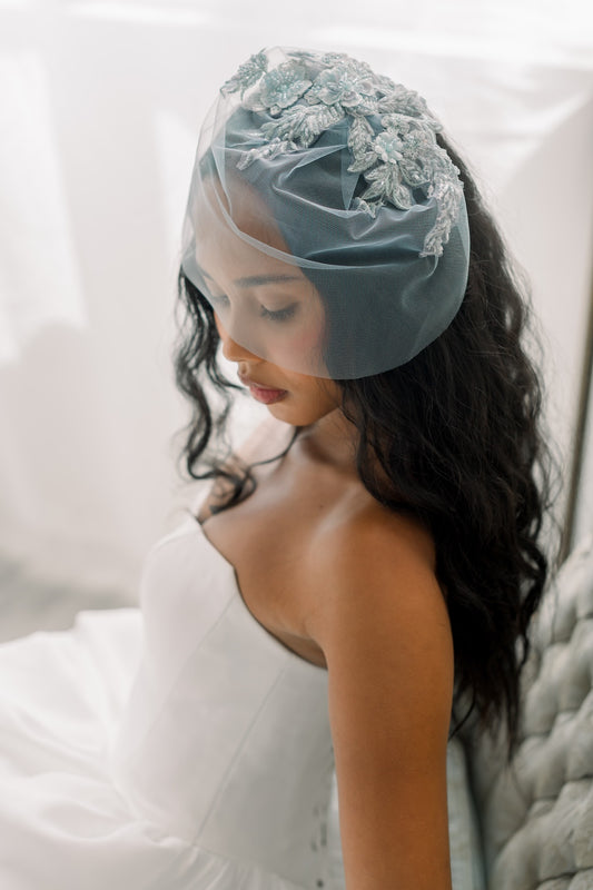 Woman wearing a light blue veil with floral lace details on a white background