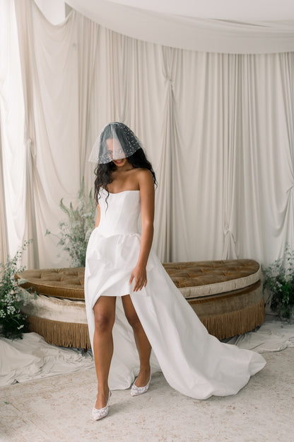 Woman in a white wedding dress with a sheer veil standing in a decorated room.