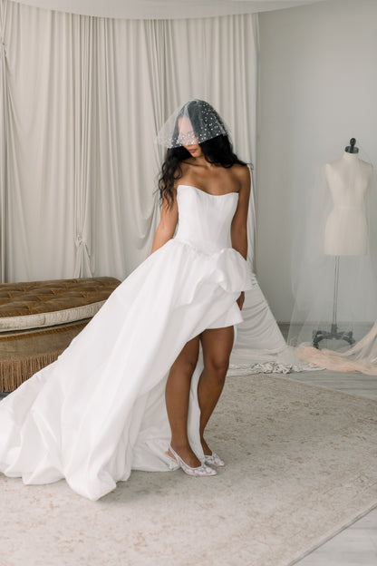 Woman in a white wedding dress standing in a room with neutral decor.
