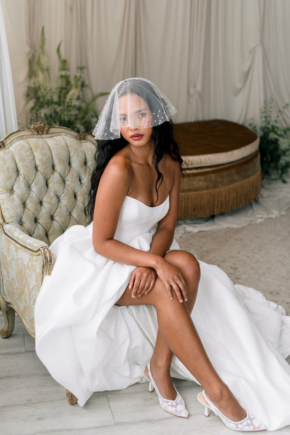 Woman in a white wedding dress with a veil sitting on a couch in a decorated room.