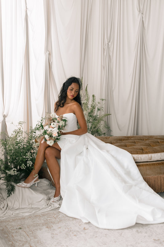 Woman in a white wedding dress sitting on a couch with floral decorations.