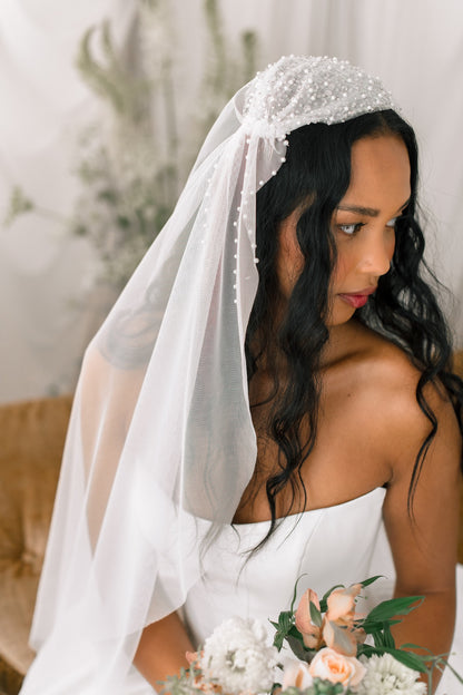 Bride wearing a white veil with a floral headpiece, holding flowers indoors.