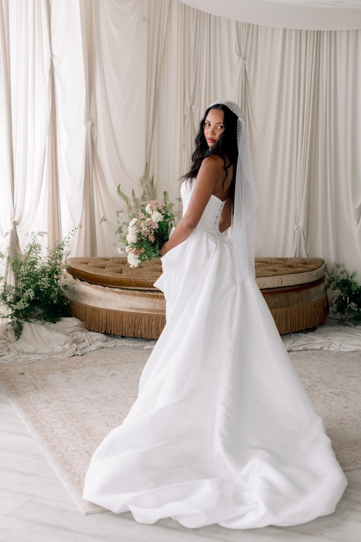 Woman in a white wedding dress standing in a decorated room with floral arrangements and a large woven basket.