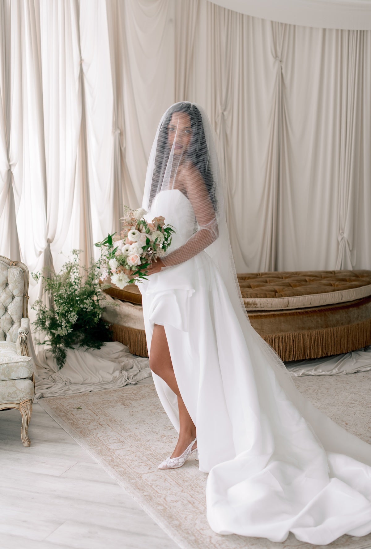 Bride in a white wedding dress holding a bouquet in a decorated room.
