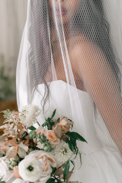 Bride holding a bouquet of flowers with a veil in the background