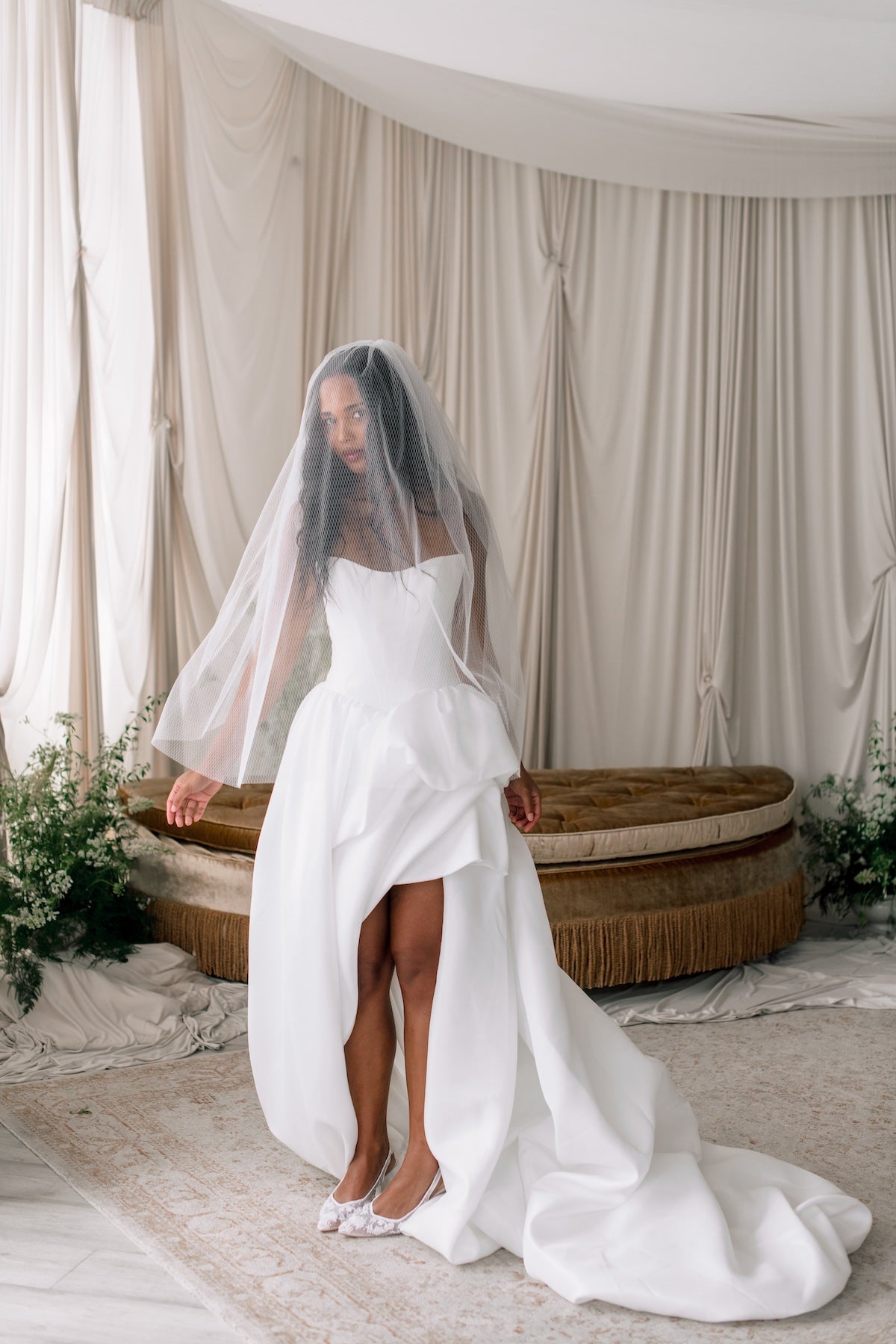 Woman in a white wedding dress with a veil standing in a decorated room.