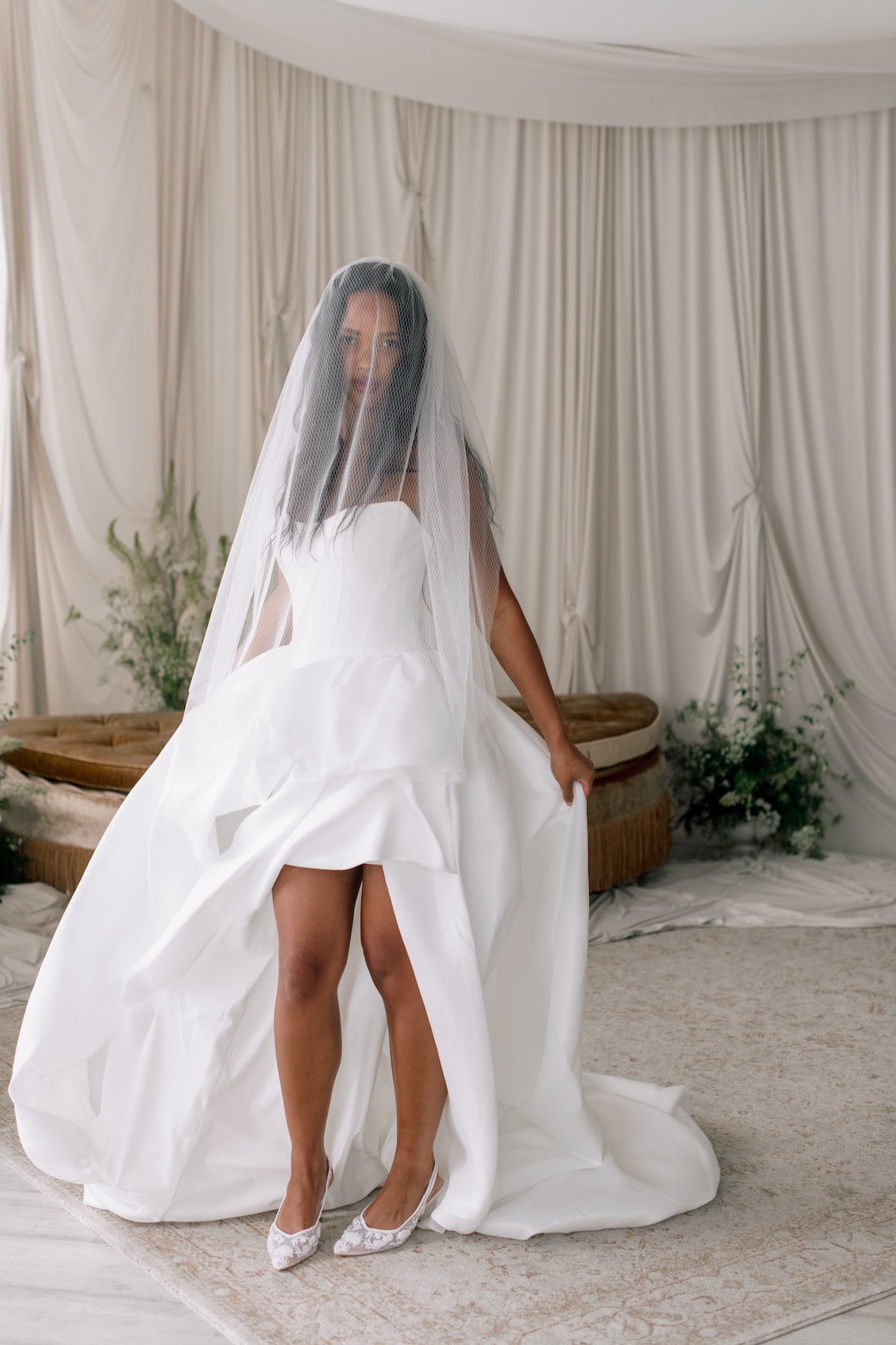 Bride in a white wedding dress with a long veil standing in a decorated room.