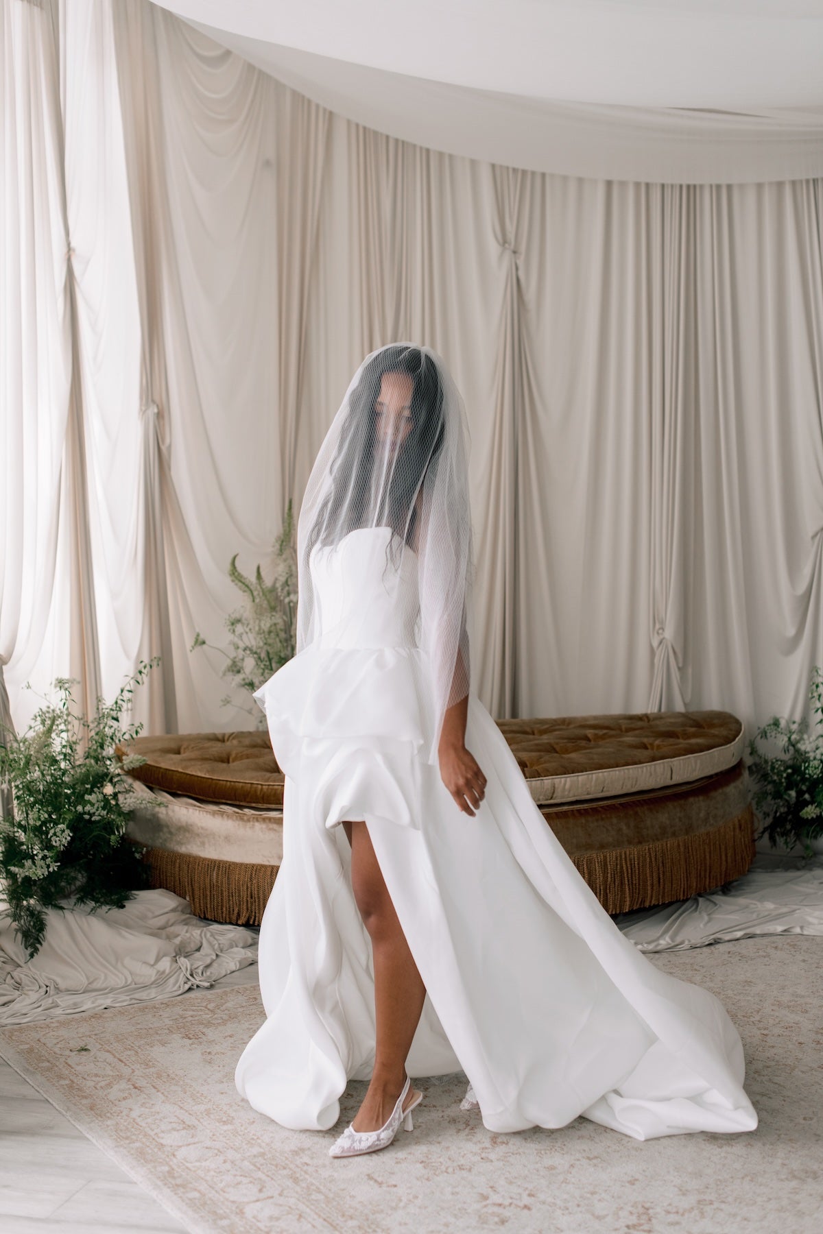 Bride in a white wedding dress with a veil standing in front of draped curtains.