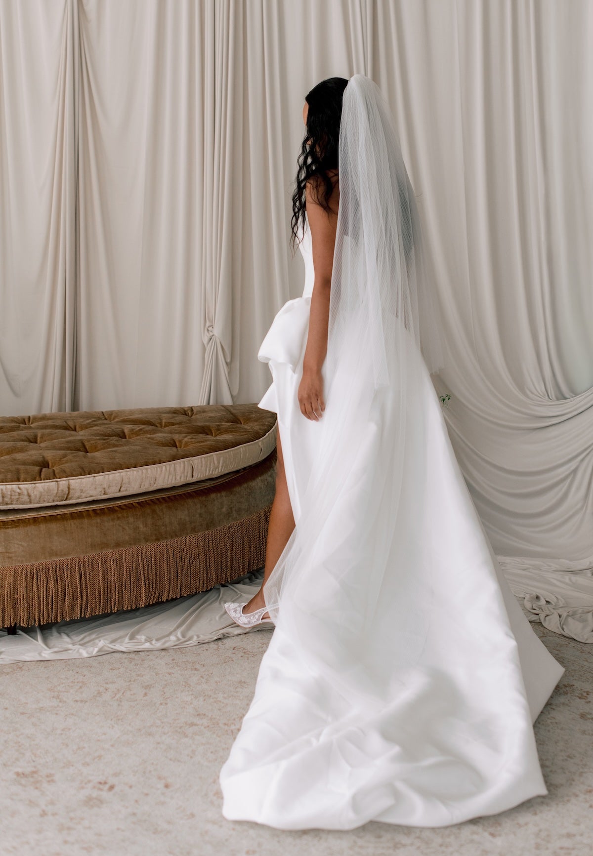 Bride in a white wedding dress with a long veil standing in front of a draped curtain.