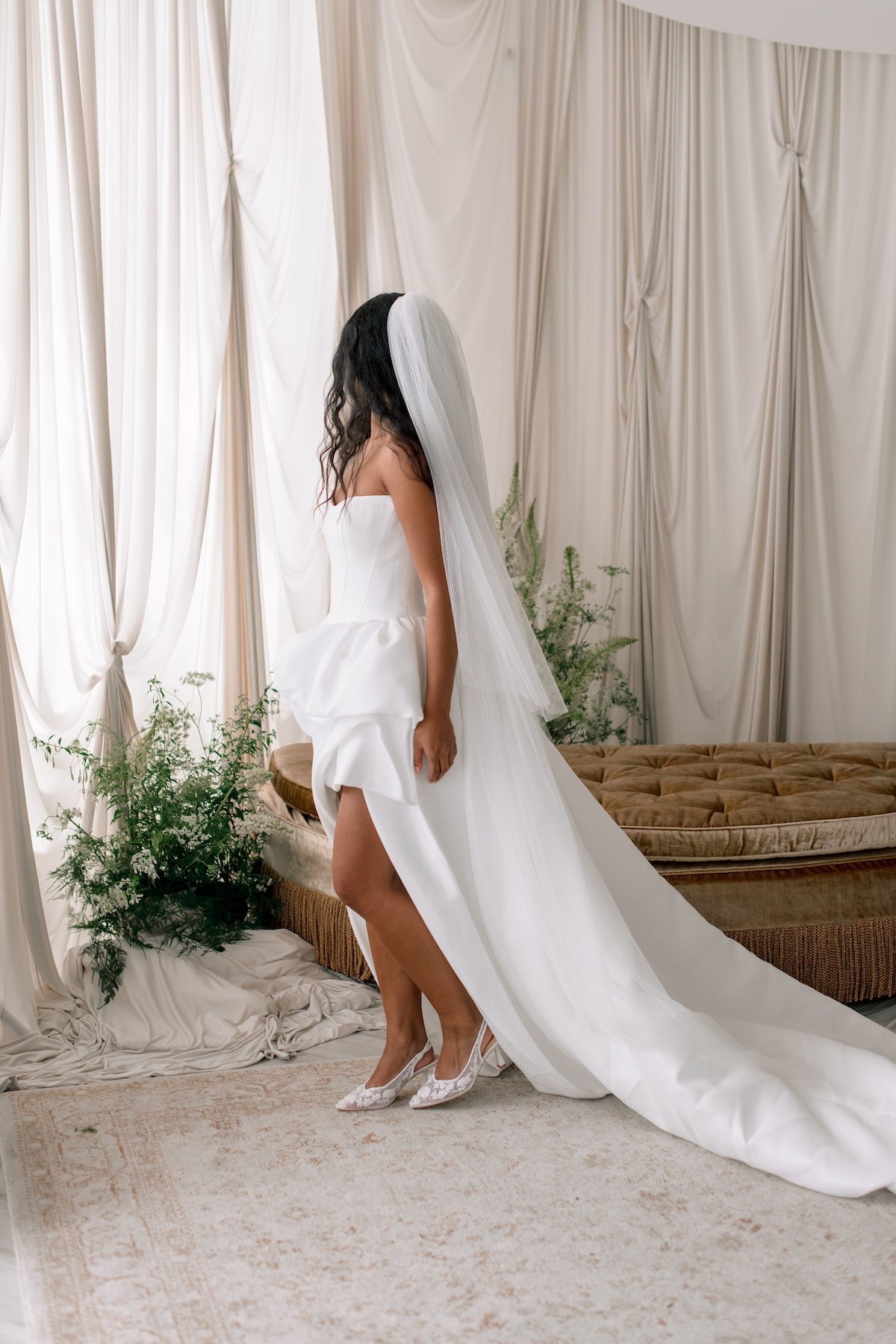 Bride in a white wedding dress with a long veil standing in a decorated room.