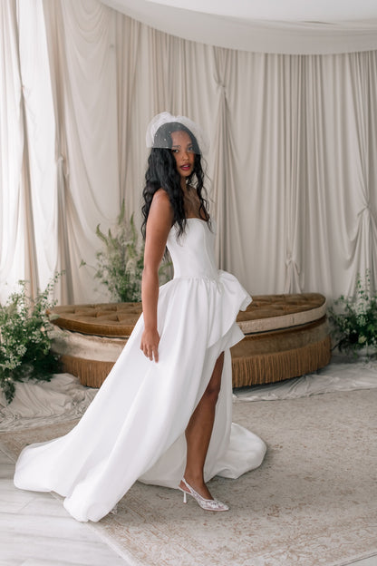Woman in a white wedding dress standing in a decorated room with curtains and plants.