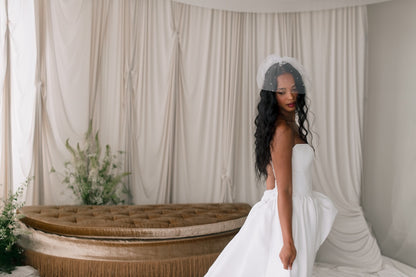 Bride in a white gown with a veil standing in front of a decorative backdrop.