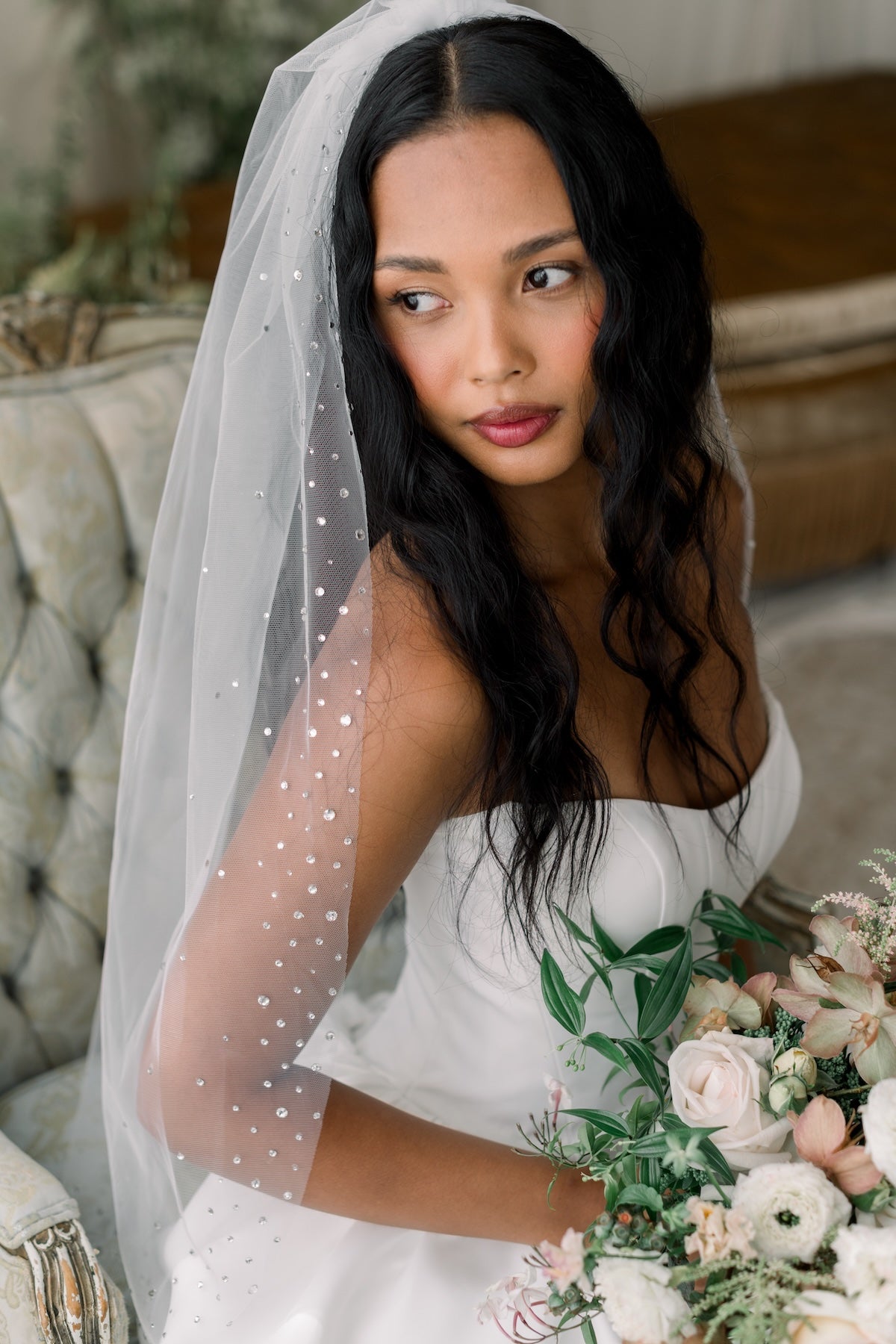 Bride holding a bouquet with a veil, sitting on a couch.
