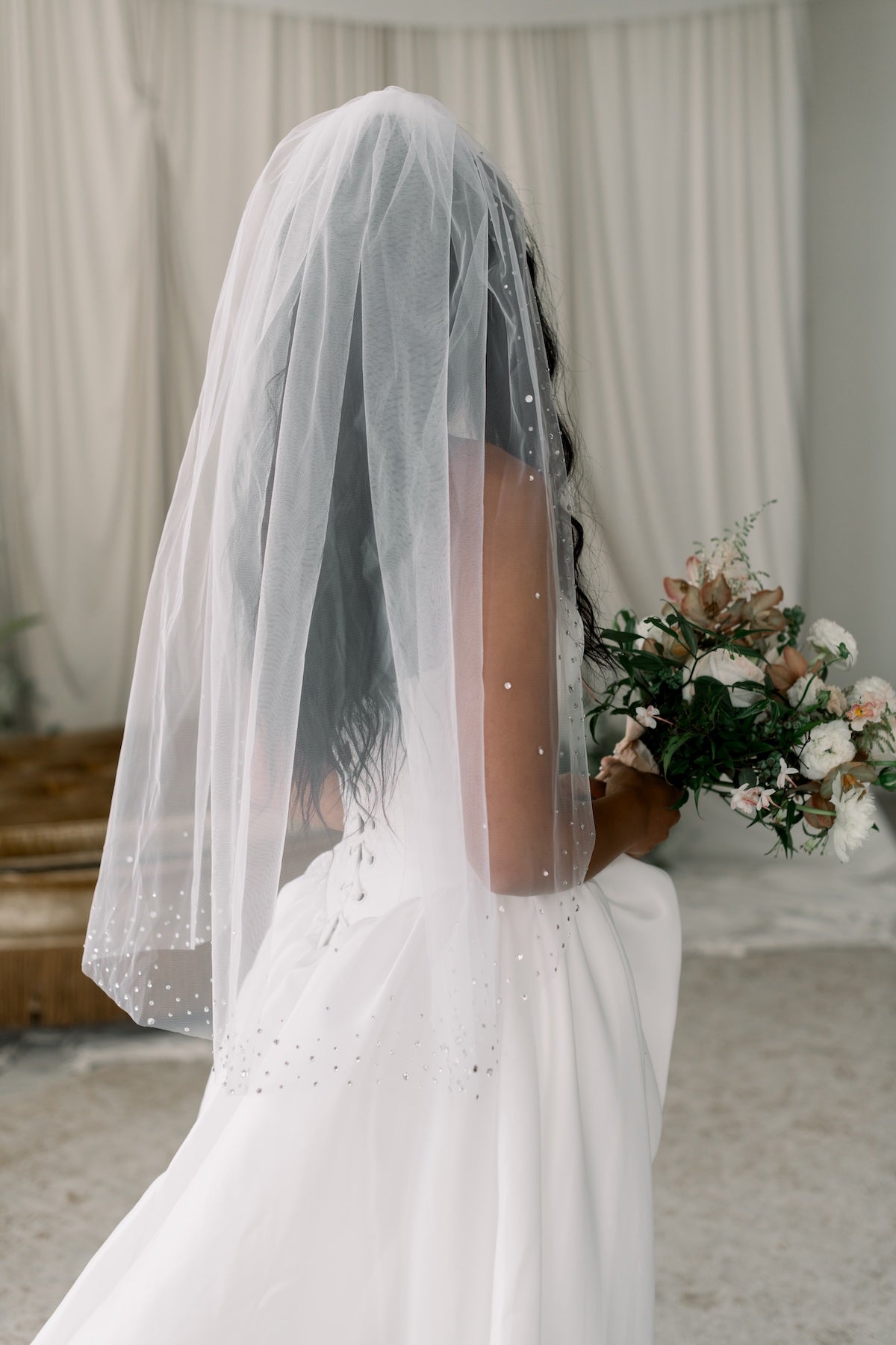 Person wearing a white veil and holding a bouquet indoors.