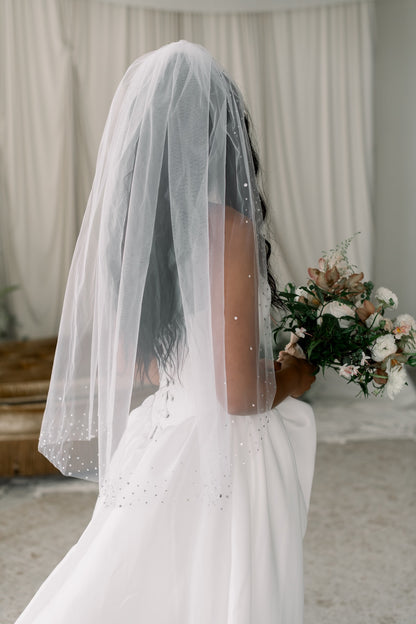 Person wearing a white veil and holding a bouquet indoors.