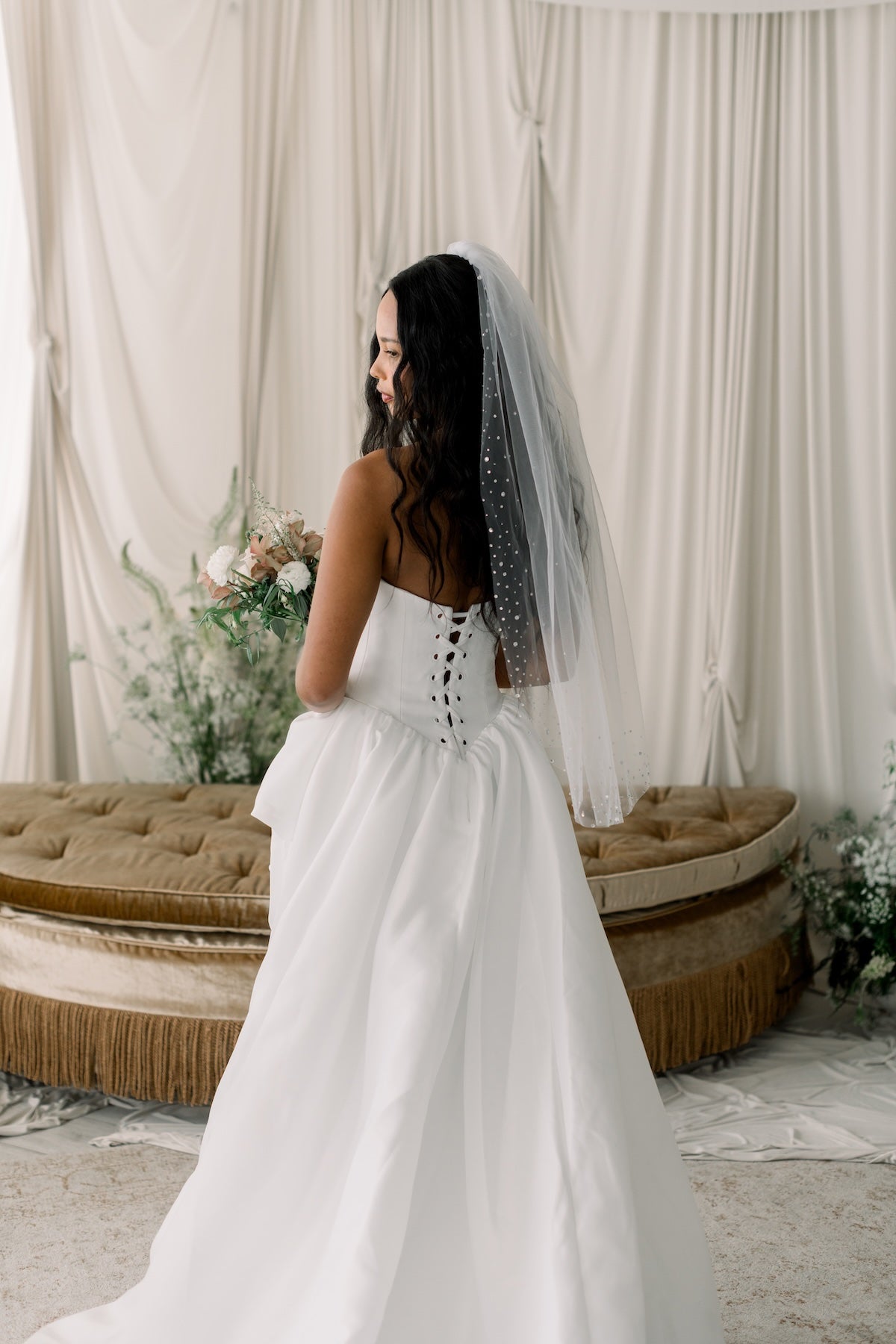 Woman in a white wedding dress with a veil standing in a decorated room.