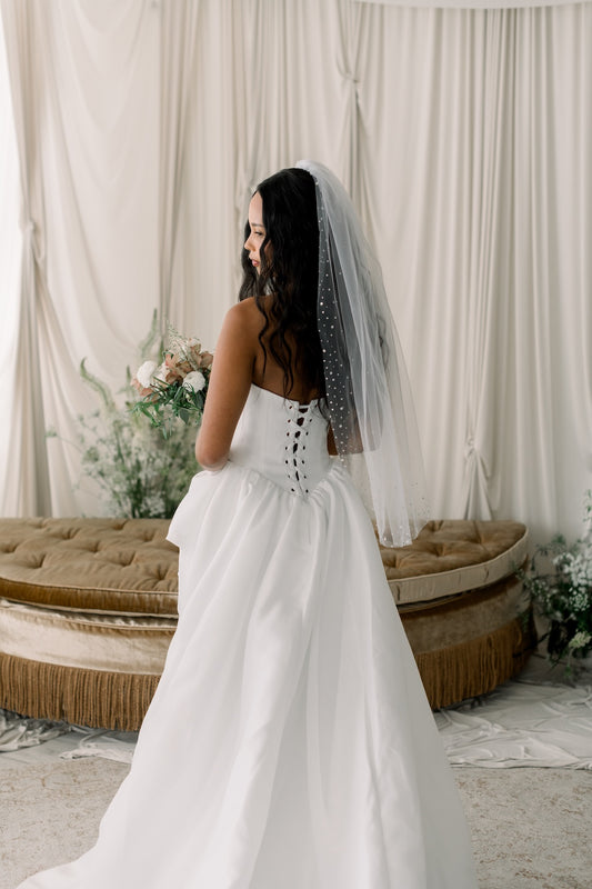 Woman in a white wedding dress with a veil standing in a decorated room.