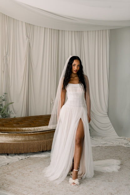 Woman in a white wedding dress with a veil standing in a room with white curtains.