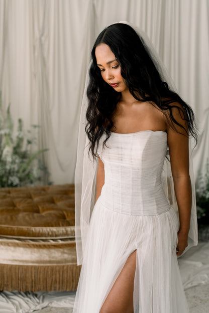 Woman in a white strapless dress with a slit, standing against a neutral background.