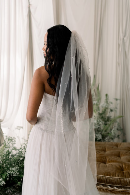Woman in a white dress with a veil standing in front of white curtains.