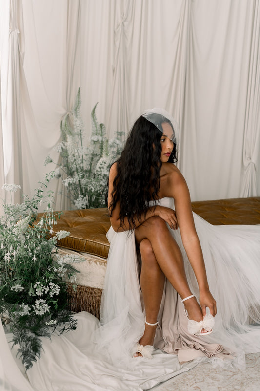 Woman in a white dress sitting on a couch with floral decorations and white curtains in the background